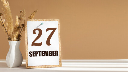 september 27. 27th day of month, calendar date.White vase with dead wood next to cork board with...