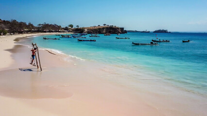 A man swinging on a swing placed on the seashore of Pink Beach, Lombok, Indonesia. The swing has...
