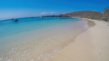 Obraz premium An areal, drone shot with a view on an idyllic Pink Beach on Lombok, Indonesia. Many boats drifting on a calm surface of the sea. Unspoiled, hidden gem. Perfect place for peaceful, relaxed holidays
