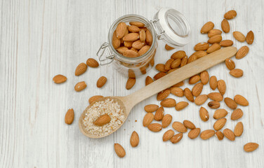 Almond nuts are poured into a glass jar and scattered on a light table. Nearby is a wooden spoon with ground almonds