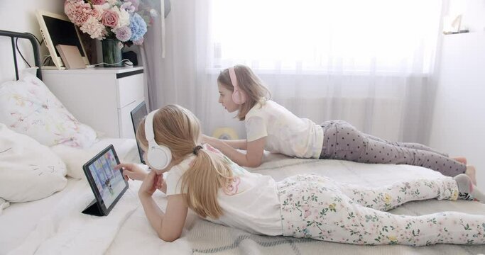 Cute kids use laptops for education, online study, home study, kids learn language online. Children play online. Video call and chat with a preschooler. Kid girls using digital tablet and headphone.