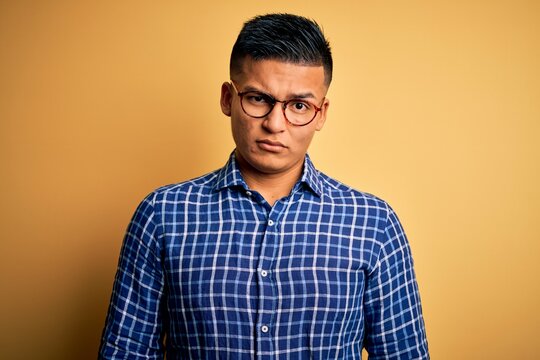 Young handsome latin man wearing casual shirt and glasses over yellow background skeptic and nervous, frowning upset because of problem. Negative person.