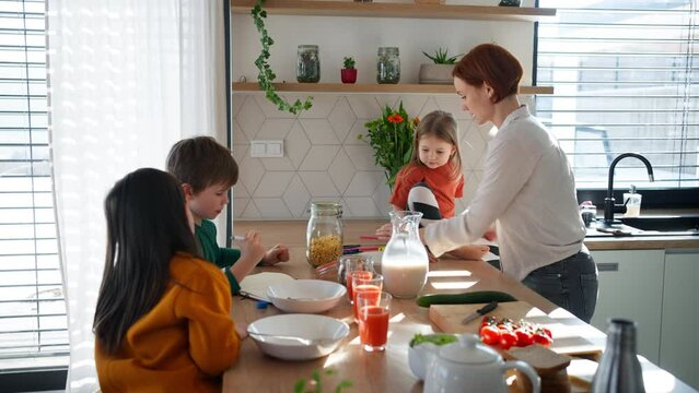 Mother of three little children preparing breakfast in kitchen at home.