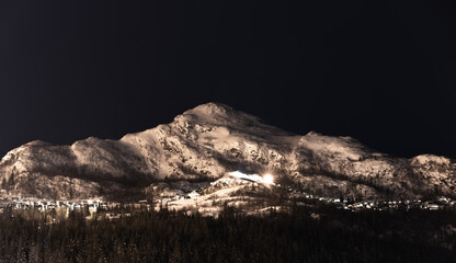 Snow covered mountain at a ski resort at night. Cabins with light in the windows.