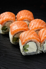 Philadelphia roll sushi with salmon, cucumber and cream cheese on black background for menu. Japanese food