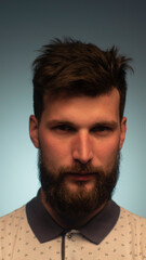 Portrait of handsome young man standing look at camera serious over blue background. Portrait of the brutal, bearded attractive young cool. Young Businessman Looking at Camera Closeup Indoors.