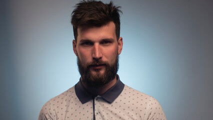 Portrait of handsome young man standing look at camera serious over blue background. Portrait of the brutal, bearded attractive young cool. Young Businessman Looking at Camera Closeup Indoors.