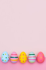Fototapeta na wymiar Easter border of vivid Easter eggs on two-tones pink background. Multi-colored striped and dotted eggs in retor style in a row with copy space.