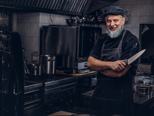 Joyful old man chef holding knife in modern kitchen