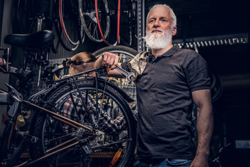 Fototapeta na wymiar Aged professional repairman posing around bicycle wheel in workshop