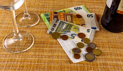 restaurant concept of cash receipt with cash change euro money, wine glasses and bottle on a brown table background