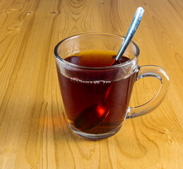 a glass cup of tea and spoon on a light wooden table background