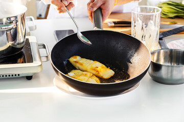 The cook is frying fish in a large frying pan. Cooking seafood in a small cafe. Close-up. unrecognizable person