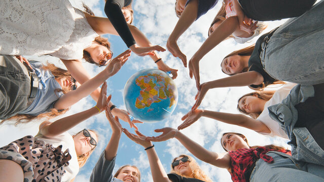 Earth conservation concept. 11 girls surround the rotating earth globe with their palms hands.