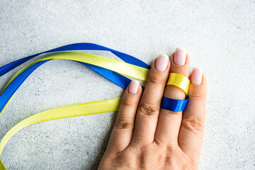 Woman's hand holding blue and yellow ribbons to symbolise solidarity with Ukraine