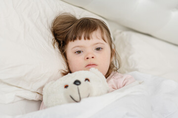 A girl with down syndrome lying on the bed under the covers and getting ready for bed. Usually childhood in a family