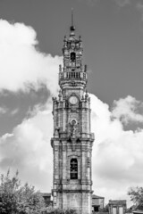 Fototapeta na wymiar Porto, Portugal: The Clerigos tower; baroque medieval tower of Clerigos church beyound trees on white clouded sky background in blacck and white