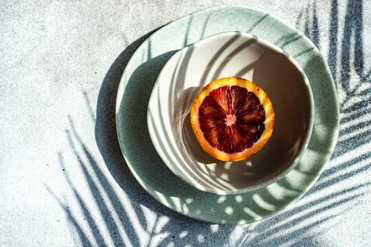 Overhead view of half a Sicilian blood orange in a bowl with a palm leaf shadow