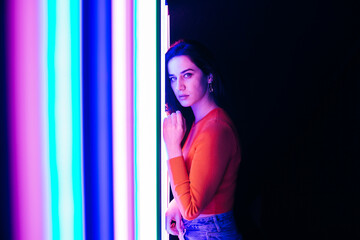 Portrait of brunette caucasian young woman with long hair, standing next to a coloured neon lights