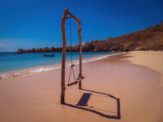 Fototapeta premium A swing on an isolated beach called the Pink Beach on the island of Lombok (next to Bali) in Indonesia. Pink and red colored corals are generating this colors.