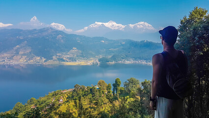 A young man looking at the Phewa Lake while hiking to the Peace Pagoda, Pokhara, Nepal. Behind the lake Annapurna Chain, with holly Mt. Fishtail.  Beautiful mountain range, clear lake surface.