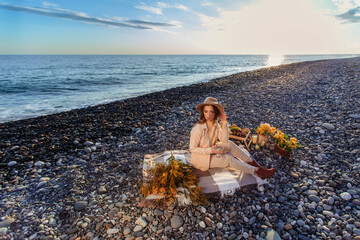 Picnic by the sea. portrait of a beautiful young woman in a hat in the rays of sunset