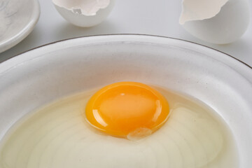 Broken egg with a yolk in a white plate. Cracked egg, eggshells with yolk. Shallow depth of field