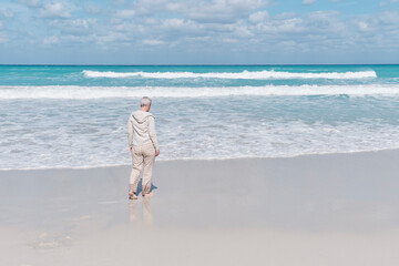 Senior woman walking alone along sandy beach of Atlantic Ocean, Varadero, Cuba.
