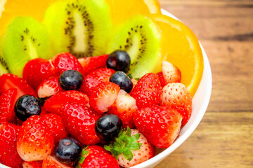 Fresh fruits concept, Fruits salad consist of kiwi and assorted berry in bowl on wooden background