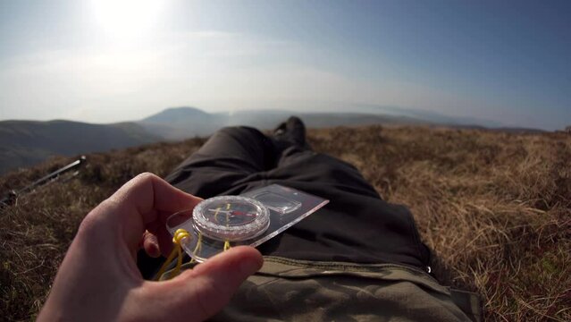 POV shot of a man using a compass while lying down in mountain grass