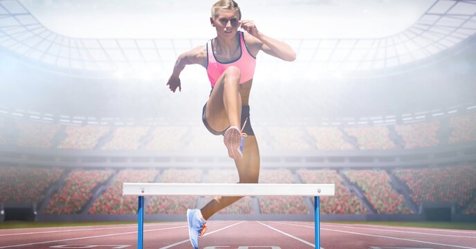 Composite image of caucasian female athlete jumping over hurdles against sports stadium