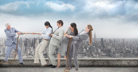 Composite image of businesspeople pulling on a rope during tug of war against view of cityscape