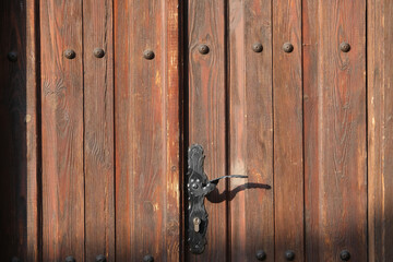 Wooden brown front door with old rusty black handle and lock closeup in sunlight as background