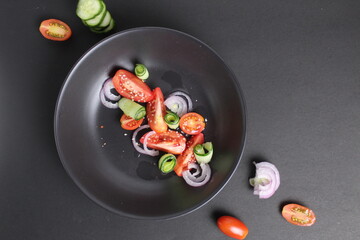 vegetable salad from tomatoes of cucumber red bluegoluke with seeds of white sesame in a black plate on a black background. Healthy food healthy lifestyle view from above