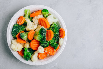 Frozen vegetables. Frozen carrots, broccoli and cauliflower in bowl on gray stone background