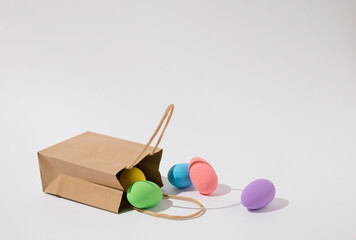 Colorful eggs falling out of a brown paper bag on white background.