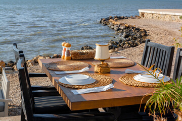 Wooden table and chairs with dishes in cafe on seashore are waiting for guests.