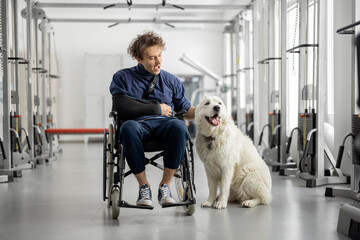 Young guy with disabilities sits in a wheelchair with his friendly dog at rehabilitation center....