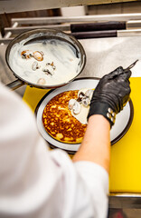 Chef's hands in gloves cooking fried pancake with mushroom sauce, bacon and egg on kitchen