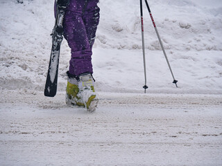Detail of the Boots and Purple Ski Pants of a Lady's Ski Suit Walking on the Snowy Road Returning after a Day of Skiing