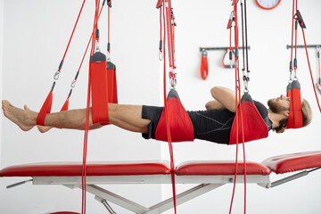 Male patient hanging on suspensions at rehabilitation center. Therapeutic exercises and...