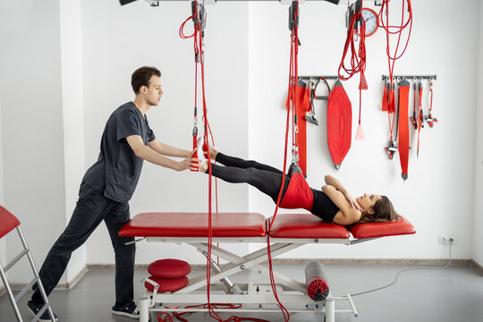 Rehabilitation specialist doing active treatment on suspension straps to female patient. Concept of therapeutic exercises to restore pain-free movement patterns and improve function