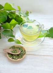 Detox birch tea in glass cup, dry and fresh birch leaves and buds on white wooden table. Betula...