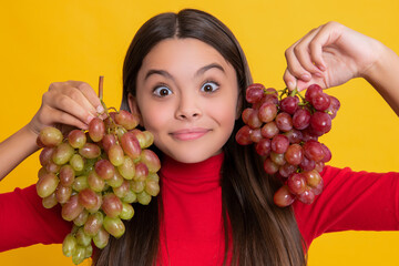 amazed positive teen girl hold bunch of grapes on yellow background