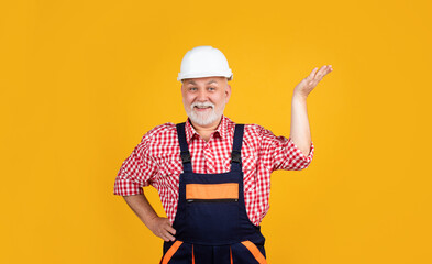 happy senior man builder in helmet on yellow background