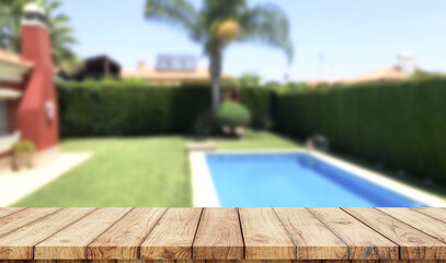 Empty wooden table with blurred luxury garden with swimming pool on background
