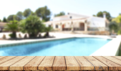 Empty wooden table with blurred luxury garden with swimming pool on background
