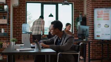 Young man analyzing business charts on laptop and files, working on financial strategy for company development and growth. Sales consultant with disability using statistics to create diagram. - Powered by Adobe