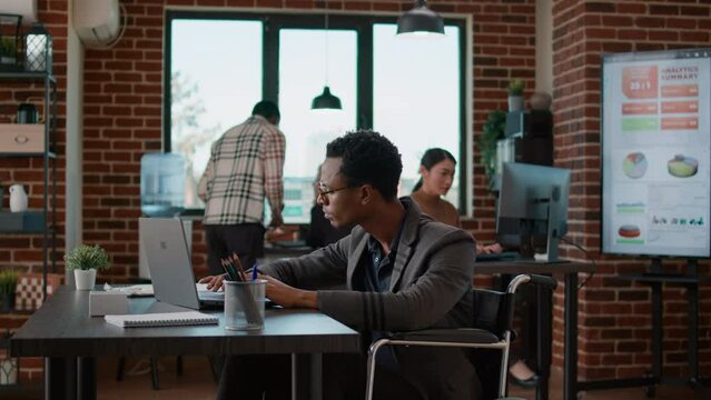Young man analyzing business charts on laptop and files, working on financial strategy for company development and growth. Sales consultant with disability using statistics to create diagram.