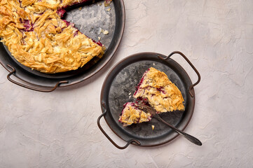 Piece of cherry pie from filo dough and fork on rustic metal tray on light background. Top view